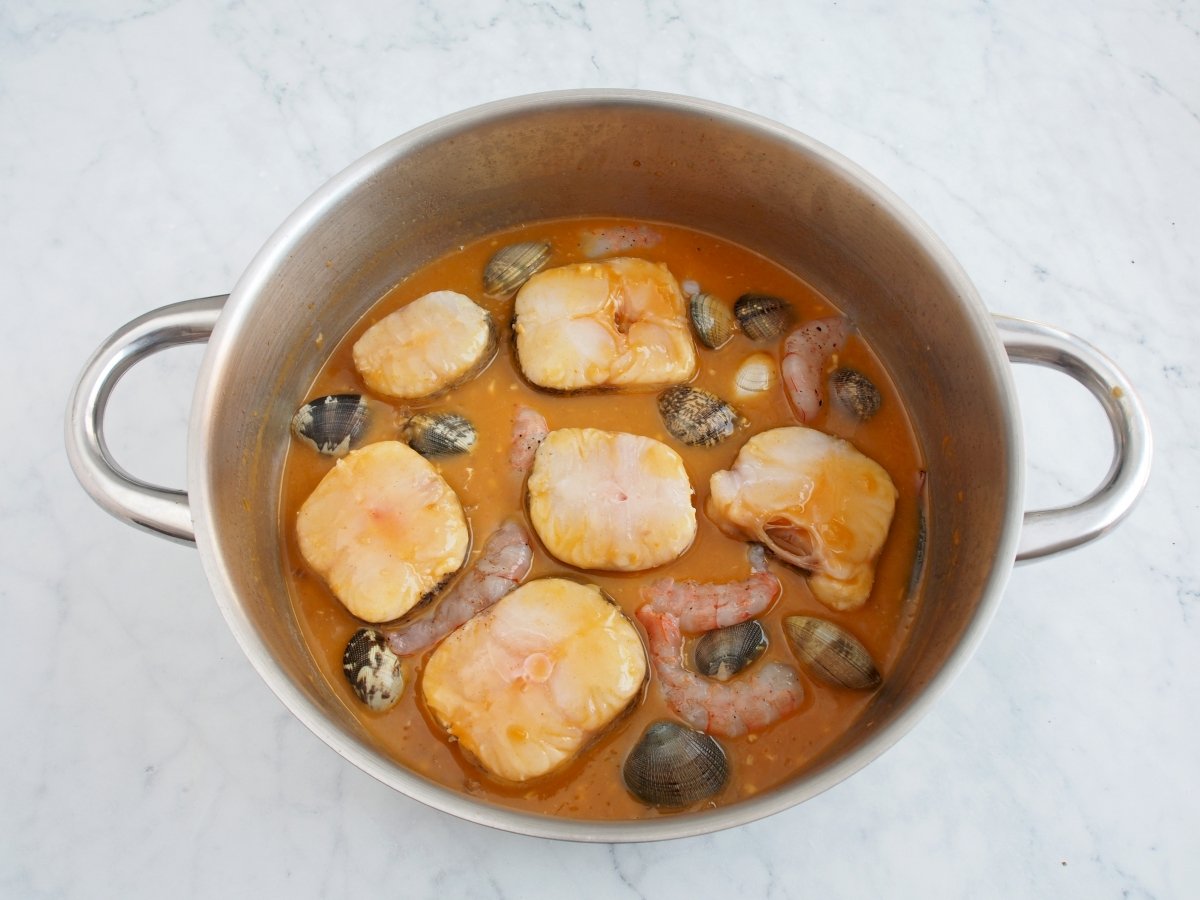 Añadir las almejas y las gambas a la cazuela de la merluza a la marinera